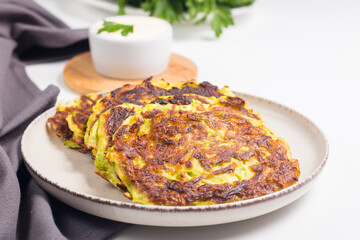 Vegetarian zucchini fritters or courgettes pancakes, served with fresh herbs and sour cream.