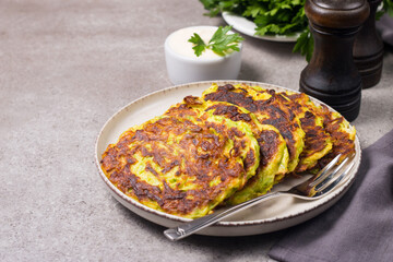 Vegetarian zucchini fritters or courgettes pancakes, served with fresh herbs and sour cream.