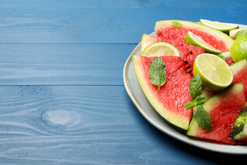 Plate with cut juicy watermelon and lime on blue wooden table, space for text