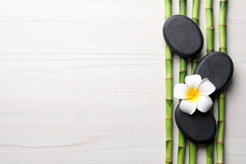 Obraz na płótnie Canvas Spa stones, bamboo stems and plumeria flower on light wooden table, flat lay. Space for text
