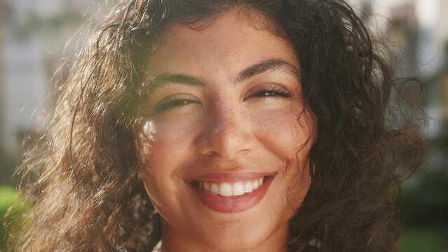 Close-up outdoor portrait of a happy young beautiful hispanic woman with curly hair.