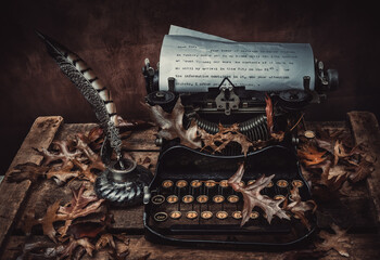 old typewriter with quill and inkwell, dried leaves cover the composition