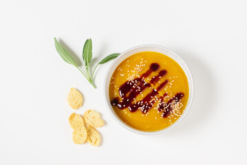 Pumpkin soup puree with sauce, sage leaves, sesame seeds in a white plate with breadcrumbs isolated