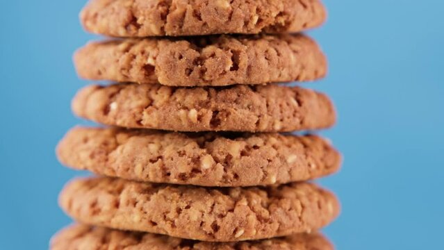 Pile of tasty oatmeal cookies with sesame seeds rotating on blue background. Rotating stack of fresh homemade cookies. Tasty bakery dessert. Food concept. Close-up in 4K, UHD