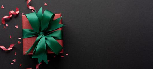 close up top view of christmas gift box with red rolling ribbon and confetti on black background with copy space for black Friday season and happy new year festival concept