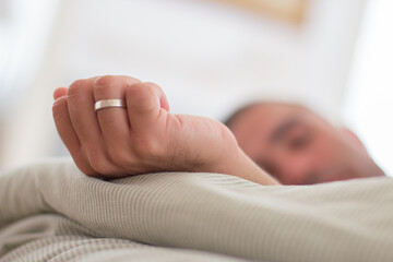 Man sleeping in bed with hand outstretched with wedding ring. Close-up shot of Caucasian mans hand with wedding ring. Man relaxing on weekend, recovering strength. Sleep cycle, engagement concept