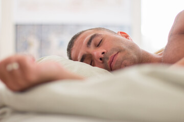 Peaceful man with naked torso sleeping on pillow in bed. Close-up shot of handsome Caucasian man having rest on weekend at home, relaxing in morning. Sleep cycle, dream concept