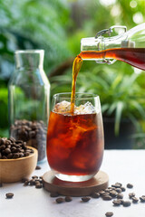 A glass of homemade cold brew coffee being pouring on bright green background