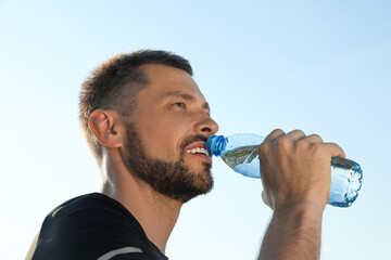 Happy man drinking water against blue sky on hot summer day. Refreshing drink