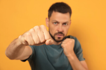 Man throwing punch against orange background, focus on fist. Space for text