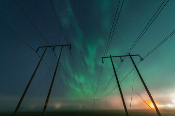Beautiful night Aurora over two double wooden pole power lines in autumn field, front view, starry...