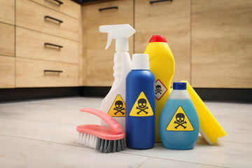 Bottles of toxic household chemicals with warning signs, scouring sponge and brush on floor indoors - obrazy, fototapety, plakaty