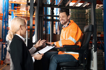 Fototapeta na wymiar Happy worker talking with manager while sitting in forklift truck at warehouse