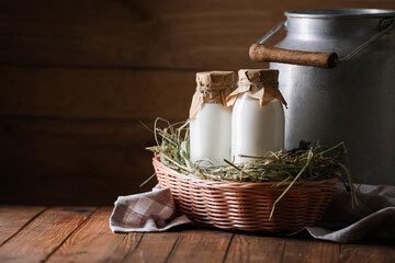 Tasty fresh milk in can and bottles on wooden table, space for text