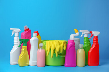 Green bucket, gloves and bottles of detergents on light blue background. Cleaning supplies
