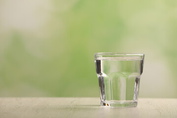 Glass of pure water on white wooden table against blurred background, space for text