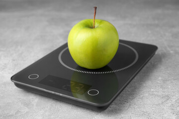 Digital kitchen scale with ripe green apple on grey table
