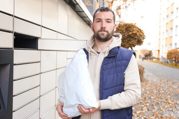 Bearded man hold parcel near self-service mail terminal. Parcel delivery machine.
