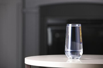 Glass of clean water on white table indoors, space for text