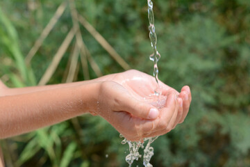 Pouring water into kid`s hands outdoors, closeup