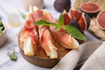 Tasty melon, jamon and figs served on white marble table, closeup