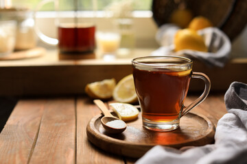 Glass cup with delicious tea, sugar and lemon on wooden table, space for text