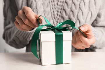 Woman decorating gift box at white table, closeup. Christmas present