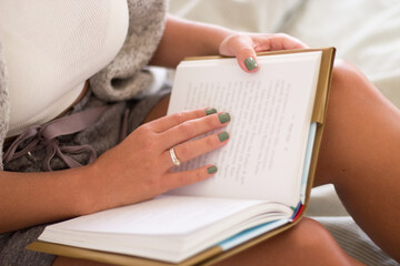 Woman sitting on bed in morning and holding book in hands. Close-up shot of unrecognizable woman in...