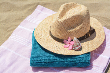 Blanket with towel, stylish straw hat and flower on sand outdoors. Beach accessories