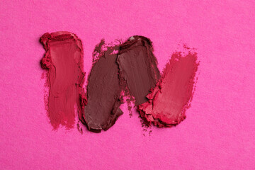 Smears of bright lipsticks on pink background, top view