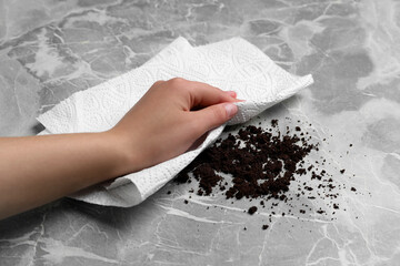 Woman sweeping scattered coffee grounds with paper towel from marble table, closeup