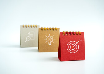 Business action plan with goal,  idea and research icon signs on small red, beige and grey desk calendar year 2023 on white background. Three step of strategy concept, minimal style.