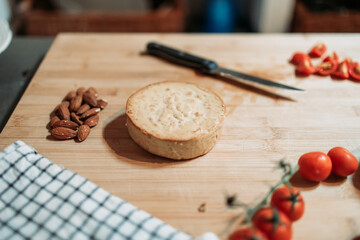 Almond cheese on the wooden board with raw almonds next to it and cherry tomato