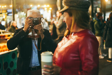 Happy senior couple having fun with vintage camera in London market - Focus on man hands