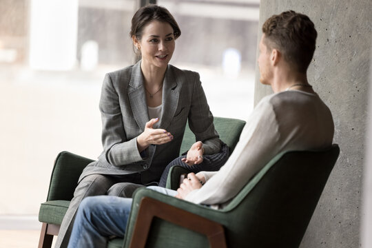 Two colleagues having good friendly conversation, talking seated on armchairs meet in office lobby, during break at workday. Businesspeople, partners solve business, share solutions and ideas indoors
