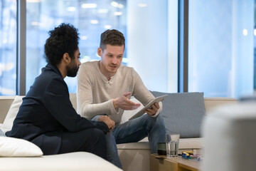 Two multi ethnic businessmen use digital tablet, discuss online presentation, startup project,...