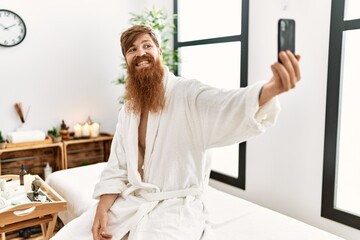 Young redhead man wearing bathrobe make selfie by the smartphone at beauty center