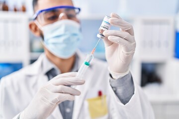 Fototapeta premium Young hispanic man scientist holding covid vaccine at laboratory