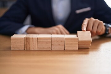 Young blond man business worker sitting on table with wooden cubes at office