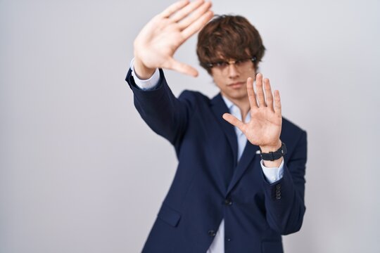 Hispanic business young man wearing glasses doing frame using hands palms and fingers, camera perspective