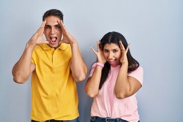 Young couple standing over isolated background smiling cheerful playing peek a boo with hands showing face. surprised and exited