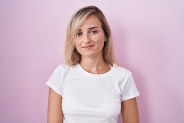 Obraz premium Young blonde woman standing over pink background smiling looking to the side and staring away thinking.