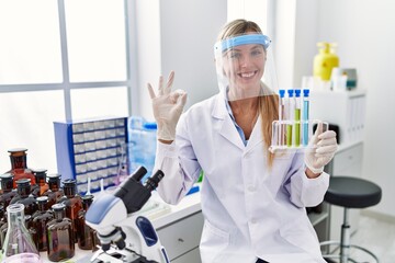 Beautiful woman working at scientist laboratory doing ok sign with fingers, smiling friendly gesturing excellent symbol