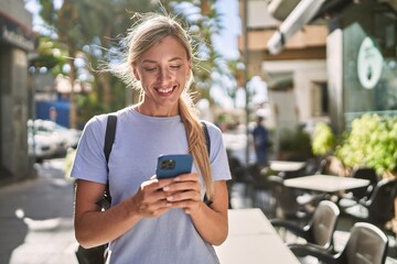 Young blonde woman smiling confident using smartphone at street