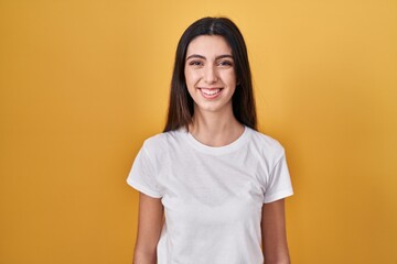 Young beautiful woman standing over yellow background with a happy and cool smile on face. lucky...