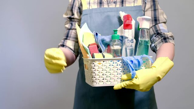 a cleaning lady holds a plastic bucket with detergents, brushes, sponges and rubber gloves for cleaning the premises.