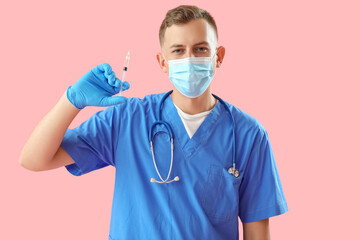 Male doctor in medical mask with syringe on pink background