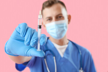 Male doctor in medical mask with syringe on pink background, closeup