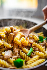 woman hand cooking tasty chicken fillet with mushroom in a creamy sauce with fusilli pasta in pan...