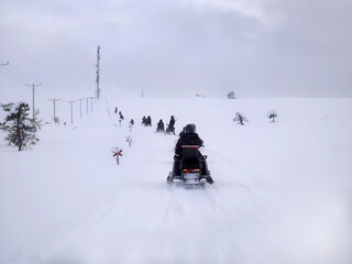 A group of tourists riding Snowmobiles on Glacier through the snowy mountains in Finland, panoramic scene of white snow hills with Pine Tree.